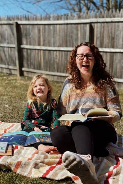 white woman and child sitting on striped blanket holding books and laughing