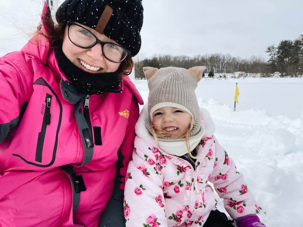 woman and child bundled up in snow gear sitting in the snow smiling